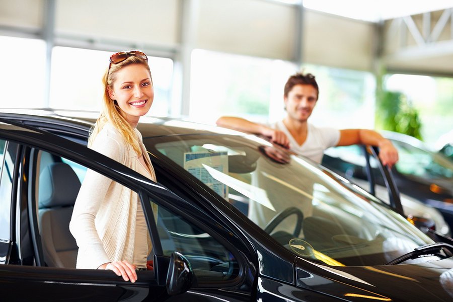 Portrait of a smiling young female with boyfriend standing by new car at showroom